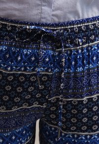 Mörkblå shorts med mönster, elastisk midja och dragsko. Har alternerande geometriska och blommiga mönster i ljusare blått och vitt.