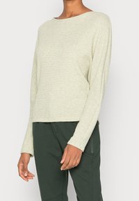 Lichtgroene lange mouwen textuurtrui met een bootnek, met een relaxte pasvorm en een rechte zoom, gedragen met donkergroene broek.