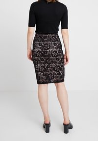 Mustat pitsimekko, jossa on kukkakuviot, slim fit -silhuetti ja suora helma. Yhdistettynä yksinkertaiseen mustaan puseroon ja tukevakorkoisiin kenkiin.