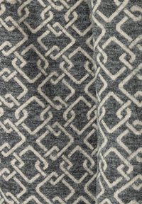 Grauer Stoff mit einem strukturierten Muster aus miteinander verbundenen cremefarbenen geometrischen Formen, das eine weiche, gestrickte Erscheinung aufweist.