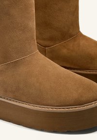 Brown suede ankle boots with a rounded toe, thick platform sole, and visible stitching detail along the midsole.