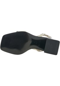 Sandaal met hak, voorzien van een zwarte rubberen zool, beige bandjes en een vierkante hak. Heeft een antislipstructuur en merklogo op de zool.