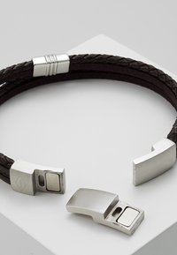 Punos ruske kože u pletenici s metalnim akcentima u srebrnoj boji i magnetnom kopčom. Sadrži elegantan, minimalistički dizajn s glatkim teksturama.