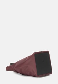 Borsa impermeabile color bordeaux con un design affusolato e una base rettangolare nera. Texture liscia con cuciture minime e bordi rinforzati.