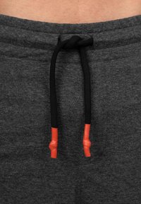 Grijze sweatpants met een zwarte trekkoord voorzien van oranje kunststof uiteinden, gemaakt van een zachte, gestructureerde stof, ontworpen voor comfort.