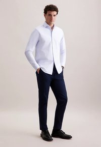 Wit overhemd met lange mouwen en een puntkraag, gecombineerd met donkerblauwe broek en zwarte schoenen. Gladde stof, op maat gemaakte pasvorm, verzorgde uitstraling.