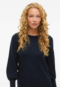 Maglione lavorato a maglia blu navy con maniche lunghe e a palloncino e scollatura rotonda. Tessuto morbido, design minimal e polsini aderenti.