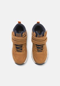 Zapatillas altas de ante marrón con forro de tela azul marino, detalles en naranja contrastantes, correa ajustable y suela de goma blanca.