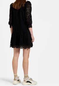 Svart spetsklänning med puffiga 3/4-ärmar, scalloped nederkant och ett strukturerat blommönster. Tillsammans med klumpiga sneakers och randiga strumpor.