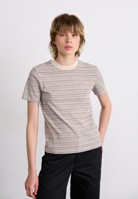 Kortærmet t-shirt i beige og brune vandrette striber, med en cremefarvet ribkant og blød tekstur. Båret med mørke bukser.