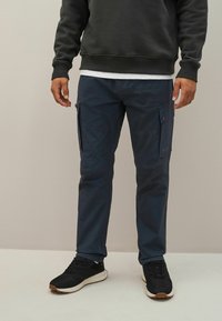 Marina cargo byxor gjorda av texturerad tyg, med sidofickor med lock, raka ben och en lös passform. Matchas med svarta sneakers.
