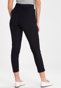 Marinblå randiga byxor med en figurnära design, avsmalnande ben och midjebälte, kombinerade med vita slip-on skor.