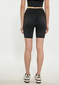 Zwarte high-waisted fietsshorts gemaakt van rekbaar materiaal, met een soepele textuur en een lengte tot halverwege de dij, gedragen met witte sneakers.