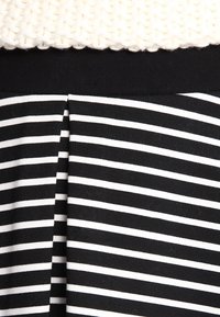 Tessuto a righe bianche e nere con una sezione superiore texturizzata. Il design presenta righe orizzontali e un dettaglio plissettato in vita.
