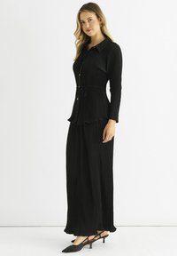 Black, ribbed maxi dress with a collared neckline, front buttons, waist tie, and flared hem. Paired with black slingback heels.
