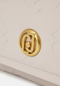 Borsa a mano beige chiaro con motivo a logo impresso, dotata di un clasp circolare in metallo dorato con un design stratificato e dettagli del marchio.