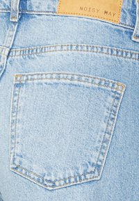 Um par de jeans de denim azul claro com um único bolso traseiro. Apresenta costura laranja e um rótulo castanho "NOISY MAY" na banda da cintura.