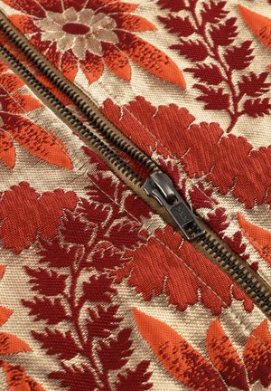 Embroidered fabric featuring large red and orange floral designs on a beige background, with a visible black metal zipper detail.