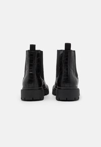 Bottines noires avec un motif crocodile brillant, des panneaux élastiques sur les côtés et une semelle en caoutchouc épaisse. Langettes à l'arrière pour un enfilage facile.