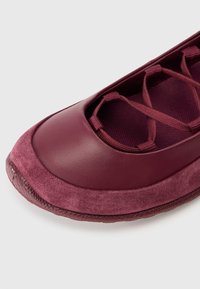 Ballettskor i djup burgundy läder och mocka, med en strukturerad kant, öppen tådesign och korslagda elastiska detaljer.