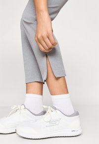 Ανοιχτό γκρι κοντά παντελόνια με φερμουάρ στο στρίφωμα, σε συνδυασμό με λευκά αθλητικά παπούτσια και ριμπ λευκές κάλτσες.