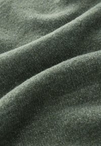 Tekstureret stof i afdæmpede grønne nuancer med et strikket mønster og subtile variationer. Blødt, varmt og let håret udseende.