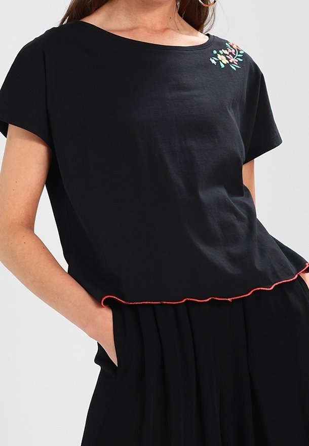 T-shirt noir à manches courtes en coton, doté d'un broderie florale colorée sur la poitrine et d'un ourlet rouge festonné.