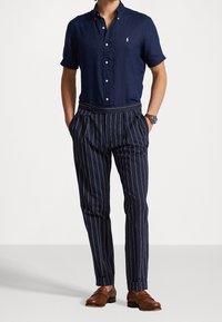 Navy linen short-sleeve button-up shirt, paired with navy pinstriped trousers and brown leather shoes. Features a subtle logo on the shirt.