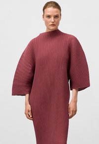 Bordeauxfarbendes, gefälteltes Kleid mit hohem Kragen und breiten, kurzen Ärmeln. Strukturierter Stoff sorgt für eine fließende Silhouette. Glatte Oberfläche an allen Stellen.