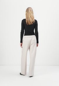 Zwarte lange mouwen top en lichtbeige wijde broek met een smocktailleband, van achteren weergegeven tegen een plain achtergrond.