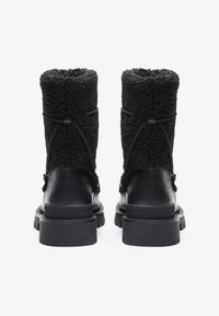 Botas de tobillo negras con una parte superior texturizada similar a la lana, base de cuero suave, punta redonda y suelas de goma gruesa. Detalle de cordón en la parte trasera.