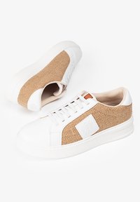Zapatillas blancas con un panel lateral de tejido beige trenzado, parte superior texturizada, punta redondeada y suela de goma blanca. Presenta costuras pronunciadas y detalle del logo.