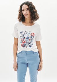 Camiseta de algodón blanca con un estampado floral en azul, rojo y rosa. Manga corta y escote redondo. Combinada con pantalones azul claro.