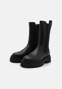 Botas de tobillo de cuero negro con paneles elásticos, punta redonda y suelas de goma gruesa con profundas ranuras para tracción.