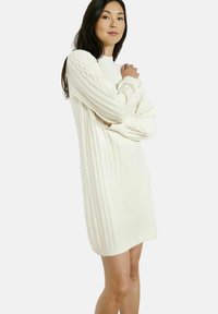 Abito bianco lavorato a maglia con motivo a trecce, maniche lunghe e vestibilità rilassata, con un collo leggermente alto e polsini a costine.