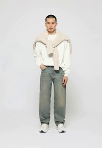 White sweatshirt, light beige knitted sweater draped over shoulders, light blue straight-leg jeans, and white sneakers.