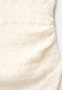 Tissu couleur crème avec un motif texturé, ondulé et froncé créant un effet froncé.