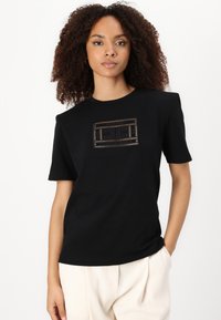 Black t-shirt crafted from soft fabric featuring a square graphic design in metallic accents. Short sleeves and a relaxed fit.