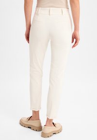 Witte, smalle broek met een gladde textuur en een mid-rise taille, voorzien van twee achterzakken, gecombineerd met beige instapschoenen.