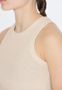 Helles beiges Tanktop mit gerippter Textur, ärmellosem Design und rundem Halsausschnitt, ausgestattet mit breiten Trägern.