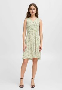 Robe sans manches à motif floral vert avec un design enroulé, taille élastique et jupe longueur genou. Sandales noires à lanières.
