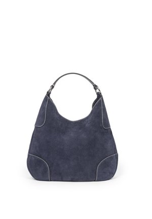Granatowa zamszowa torebka na ramię z zakrzywionym górnym uchwytem, białymi przeszyciami i zaokrąglonym, lekko trapezowym kształtem.