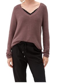 Pull en maille texturée couleur mauve avec col en V et manches longues. Superposé à un caraco en dentelle noire, accompagné d'un pantalon noir à cordon de serrage.