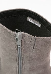 Botín gris con una textura de ante suave; cuenta con una cremallera lateral, un ligero acolchado en el collar y una etiqueta de marca en el interior.