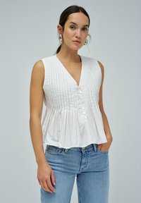 Blusa sin mangas blanca con pliegues verticales, escote en V y cierre de botón. La tela tiene una textura suave y un diseño fluido.