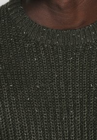 Dunkelgrüner gestrickter Pullover mit einem strukturierten Rippdesign, das über die gesamte Fläche helle Farbtupfer aufweist. Rundhalsausschnitt mit dickem Rand.