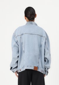 Svetlo modra prevelika denim jakna s ostrim ovratnikom, spuštenimi rameni in rjavim usnjem označbo na hrbtu, ki se ponaša z udobnim krojem.
