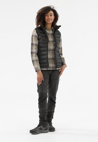 Schwarze gepolsterte Weste, karierte beige und grüne Hemdbluse, dunkle Hose und robuste schwarze Wanderschuhe. Eignet sich für Outdoor-Aktivitäten.