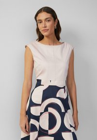 Top met cap-sleeves, aansluitend in lichtroze, overgaand in een marineblauwe rok met cirkelvormige witte en rode patronen. Gladde textuur, gestructureerd ontwerp.