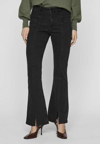 Melnas izsistās džinsus ar augstu jostasvietu, izgriezumiem pie potītēm un mīkstas tekstūras džinsu audumu. Saskaņoti ar vērpjo bordo krāsas augstpapēžu kurpēm.